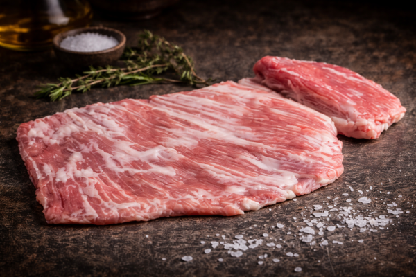 Raw pork ribs on a dark kitchen surface with salt and rosemary sprigs in the background, ready for seasoning/ cooking.
