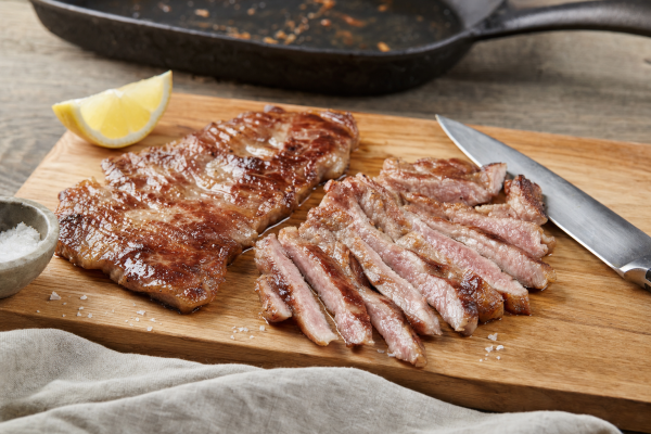 Pan-seared Ibérico secreto sliced across the grain on a wooden board, with lemon, salt and a cast-iron skillet nearby.